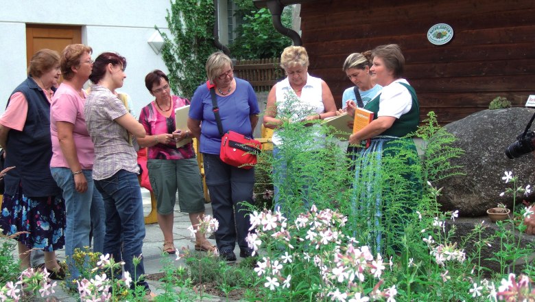 Gruppe von Frauen in einem Kr&auml;utergarten, die einer F&uuml;hrung lauschen.